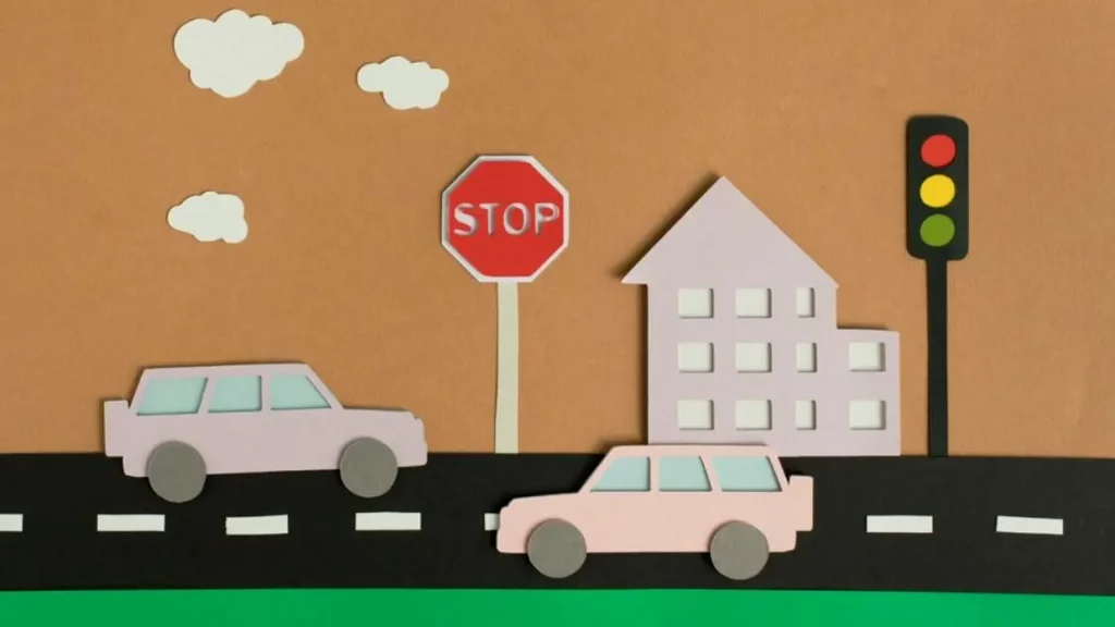 Karya seni dari kertas yang menggambarkan dua buah mobil dari arah yang berbeda di jalan raya dengan rambu lalu lintas STOP, lampu lalu lintas, dan sebuah gedung