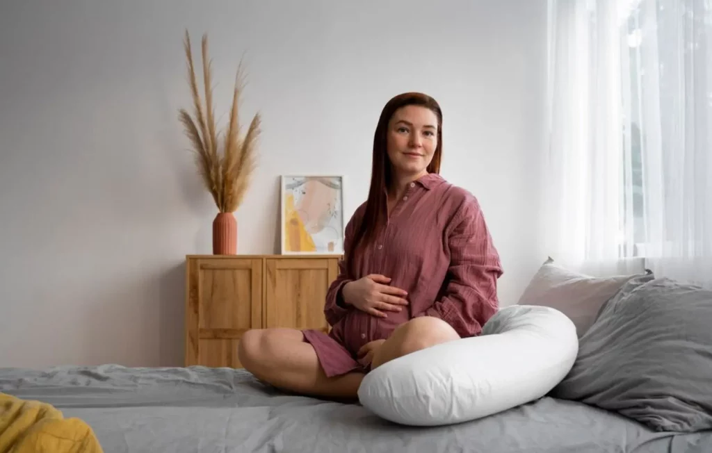Seorang ibu hamil sedang memegang perut diatas kasur